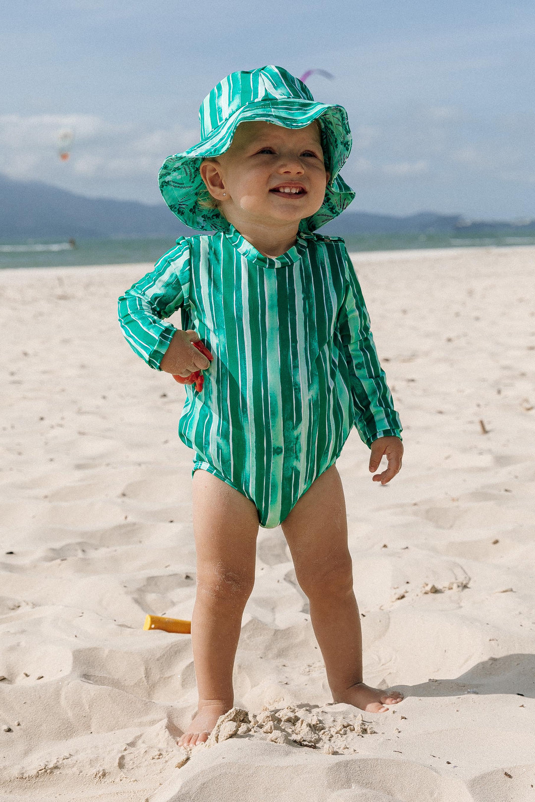 Look Moda Praia para Bebês combinando, Body e Chapéuzinho com Proteção UV, com Dupla face na estampa Lavanda, nas cores tropicais estampados Listras Verdes, da Lili Sampedro.