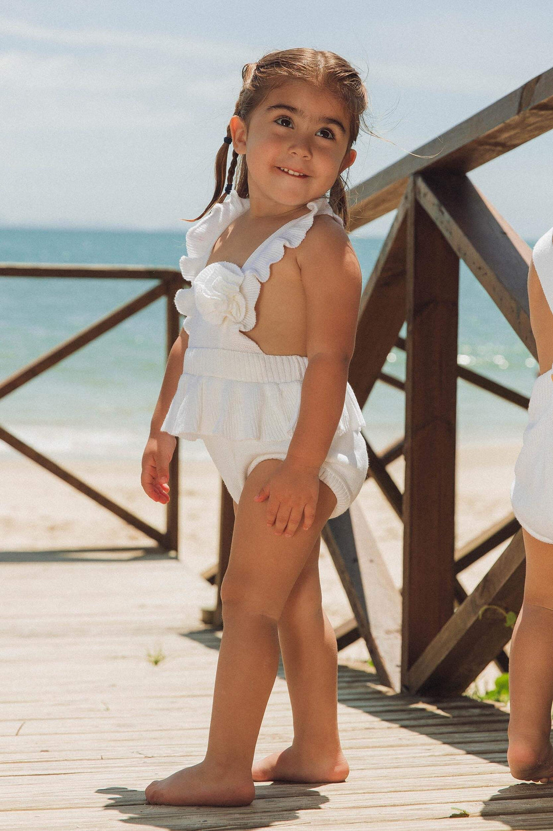 Bebê na praia usando body de tricot com aplicação de flor e babados, muito charmoso na cor Branca, perfeito para o ano novo