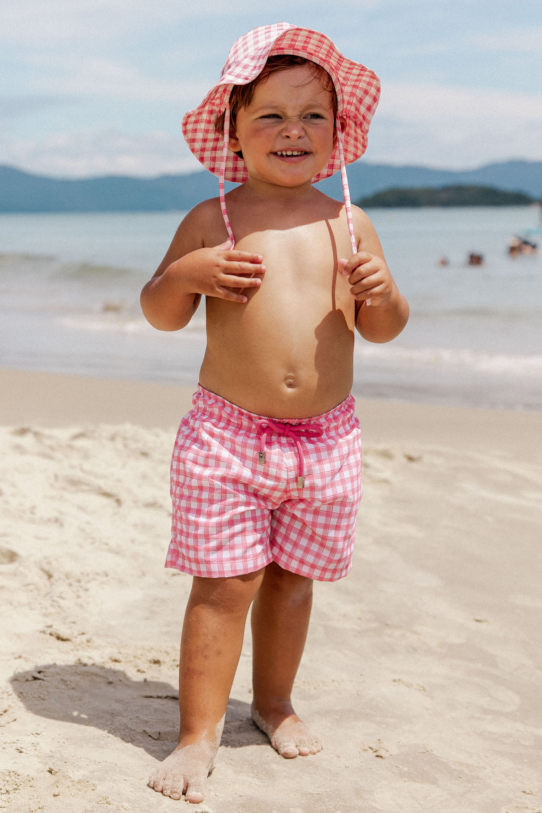  Moda Praia Infantil Masculino, look perfeito para crianças, permite criar opções para usá-lo. Short com fechamento por velcro, ajustável por cordão e bolsos funcionais, e Chápeuzinho com Proteção UV, garantindo liberdade de movimento e estilo para os pequenos aproveitarem cada momento da Praia. Na Estampa, Vichy Rosa, da Lili Sampedro.