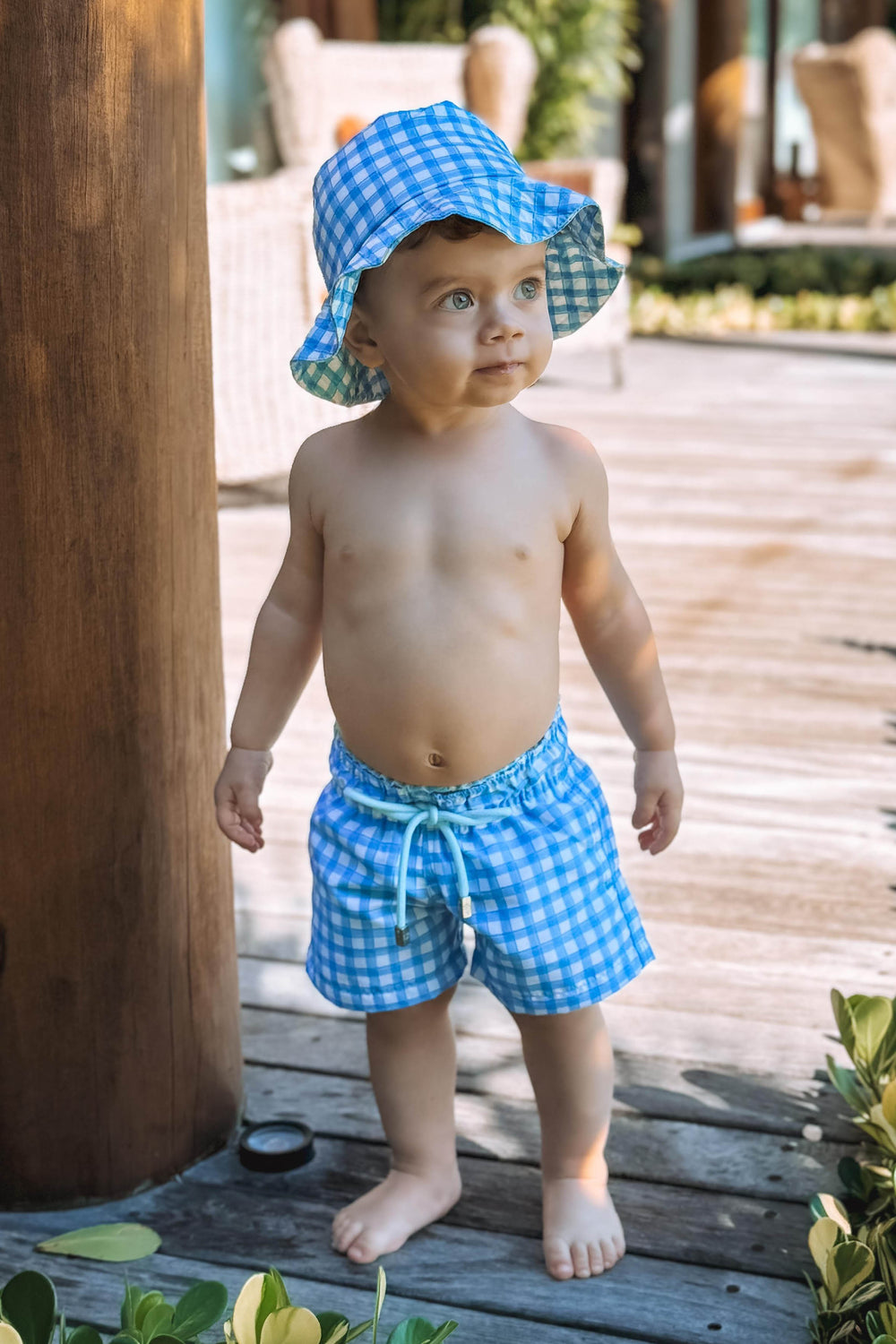 Bebê vestindo short de banho e Chapeuzinho dupla face com proteção UV na estampa Vichy Azul (Xadez), da Lili Sampedro