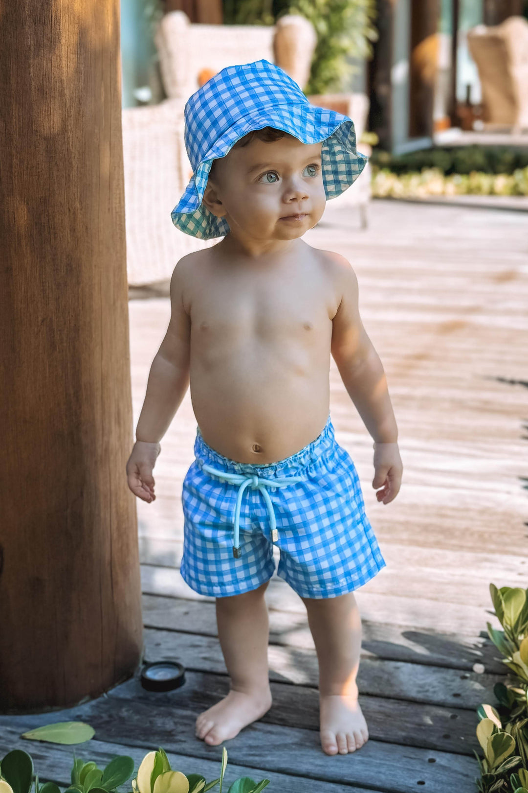 Bebê vestindo short de banho e Chapeuzinho dupla face com proteção UV na estampa Vichy Azul (Xadez), da Lili Sampedro