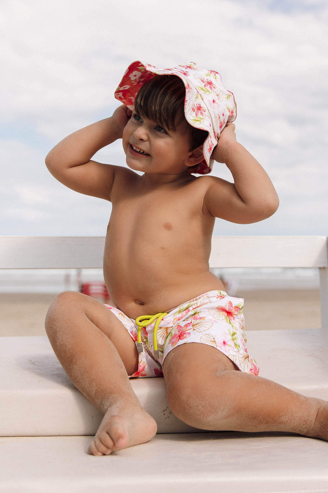 Moda Praia Infantil Masculino, look perfeito para crianças, permite criar opções para usá-lo. Short com fechamento por velcro, ajustável por cordão e bolsos funcionais, e Chápeuzinho com Proteção UV, garantindo liberdade de movimento e estilo para os pequenos aproveitarem cada momento da Praia. Na Estampa exclusiva, Hibiscos Off White, da Lili Sampedro.