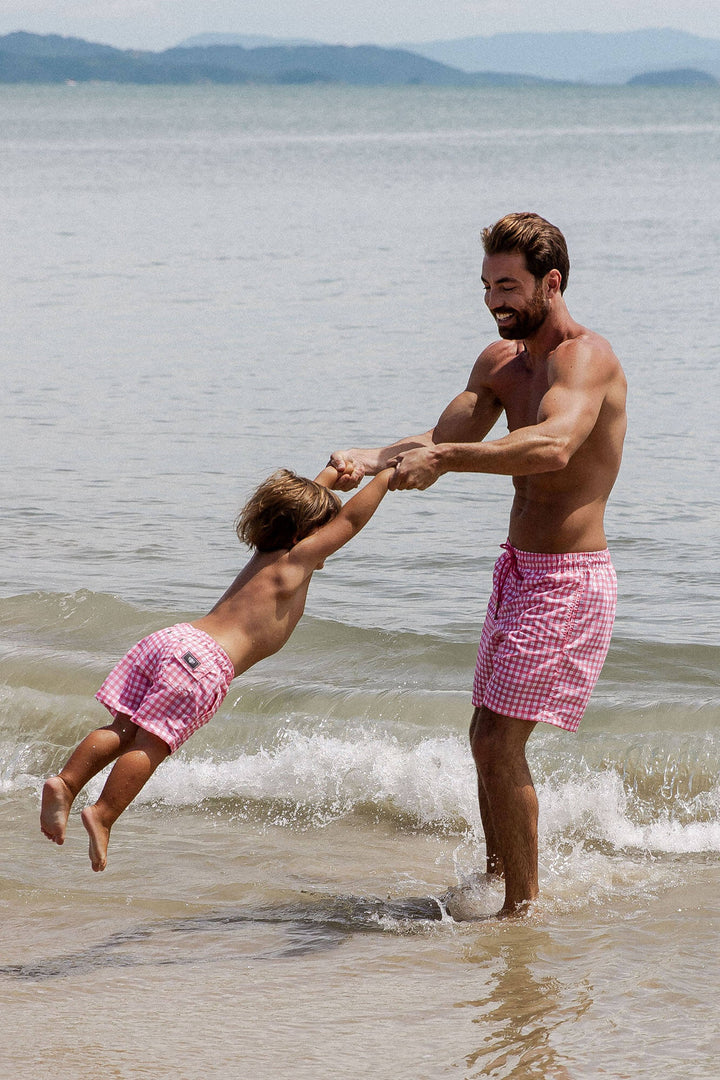 Pai e Filho brincando na praia com short de praia combinando na mesma estampa Vichy Rosa (Xadrez) Lili Sampedro.